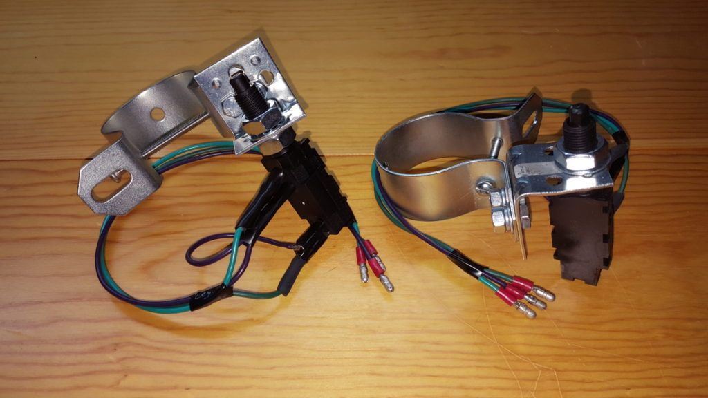 Two automotive ignition modules with metal brackets and wiring, likely for installation. They rest on a wooden surface.