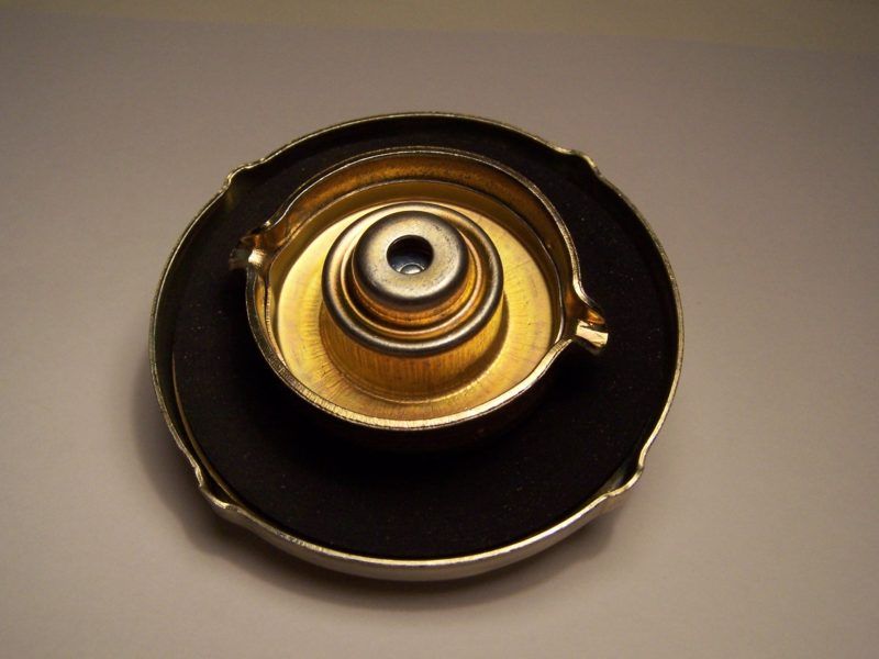 A gold-colored radiator cap with a black gasket and silver trim, viewed from above.