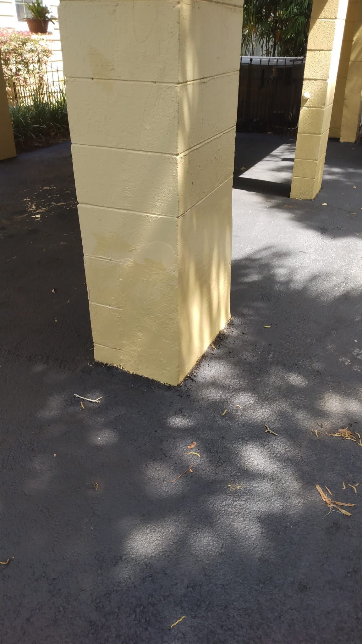 Yellow stucco column on a shaded asphalt walkway with dappled sunlight and nearby pillars