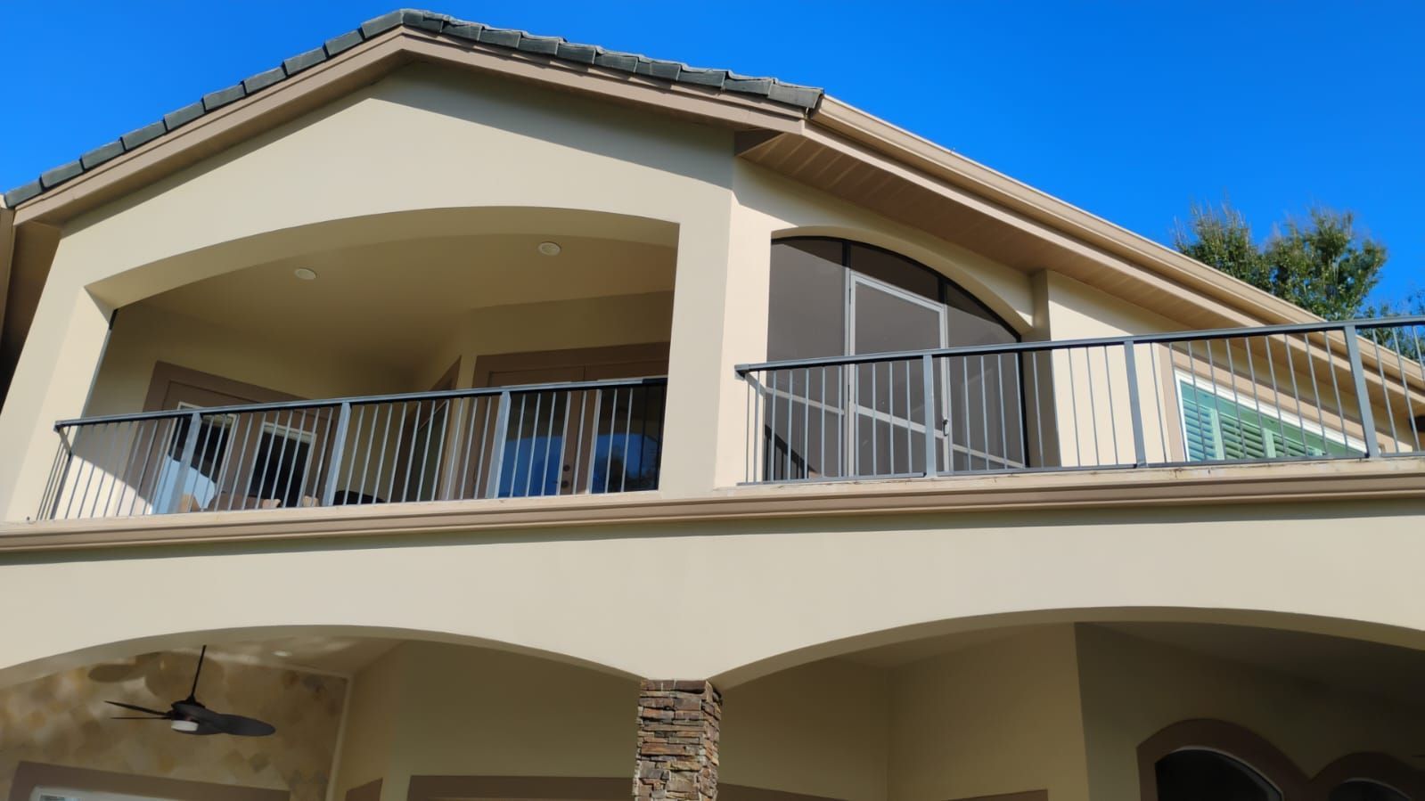 Two-story beige house with arched balconies and a tiled roof under a blue sky