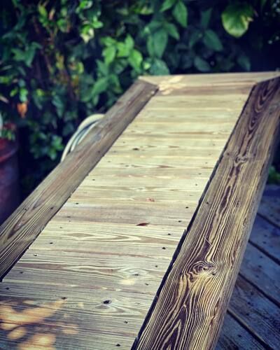 Wooden coffin resting on an outdoor deck, with green foliage in the background.