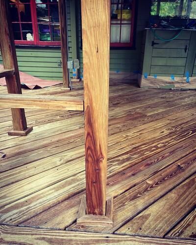 Wooden porch deck with a central support post, green siding, and a window in the background