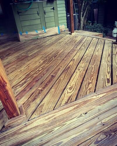Wooden deck with diagonal planks beside a house and railing, lit by daylight.