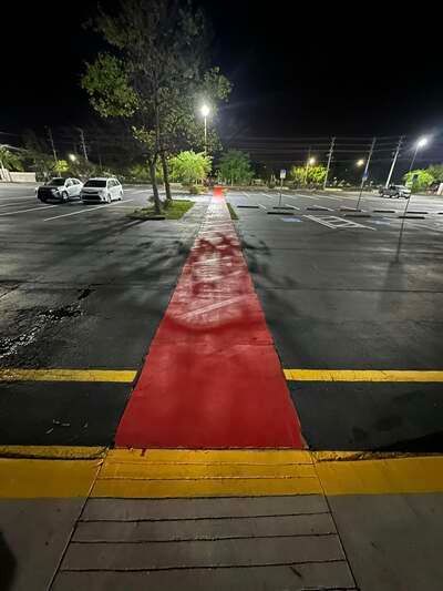 Red carpet runner across a dark parking lot at night, leading toward distant streetlights.