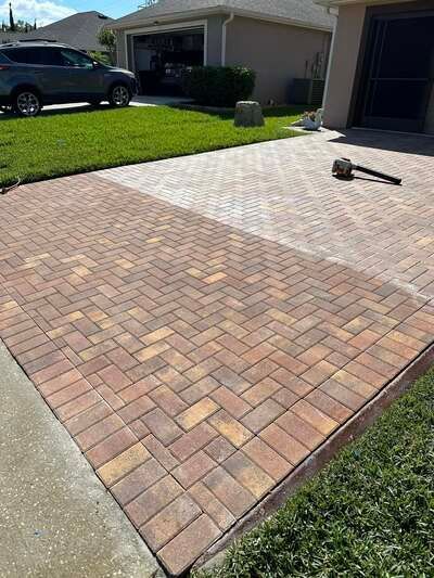 Brick paver driveway in front of a suburban house with a dark vehicle parked nearby.