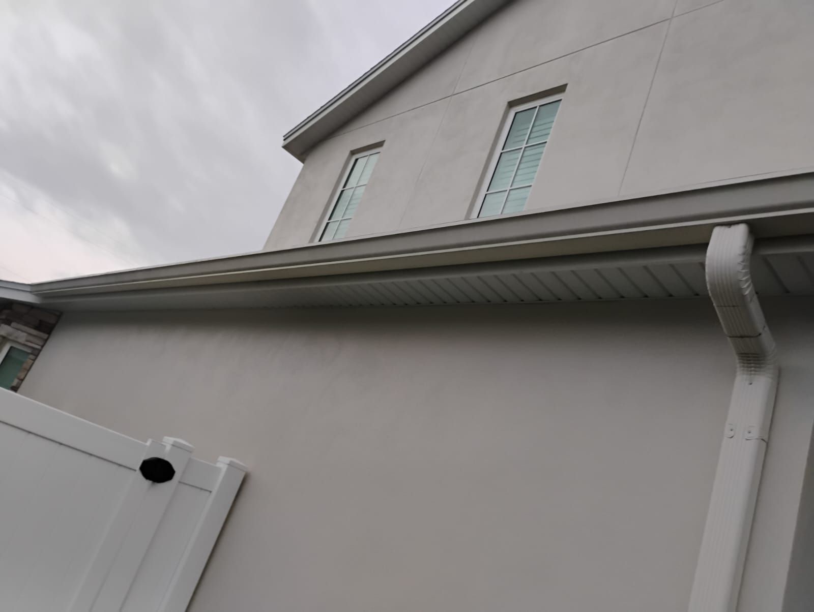 Gray house exterior with white gutter and downspout against a cloudy sky