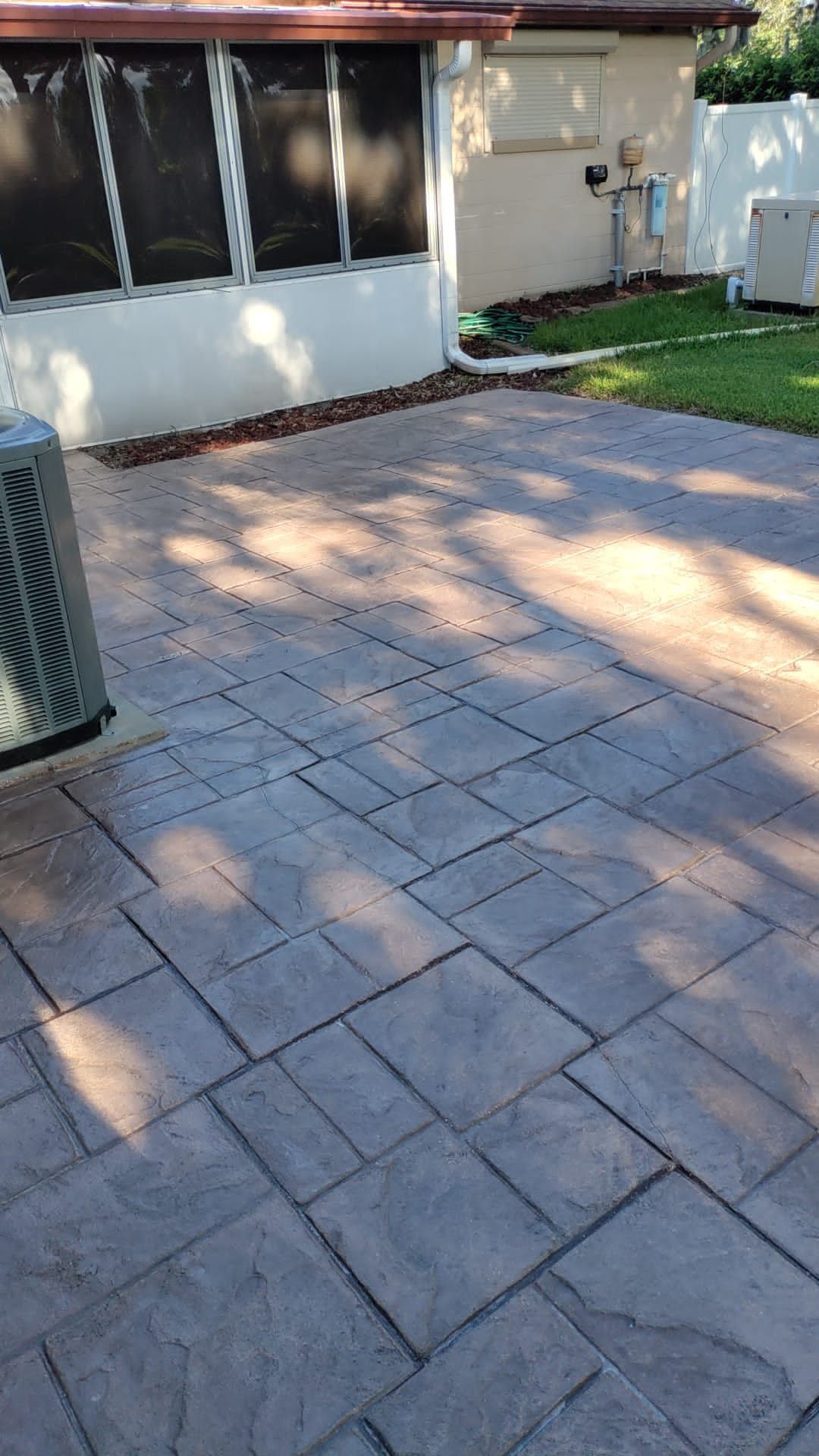 Back patio with gray pavers, house wall, windows, and a patch of grass in sunlight