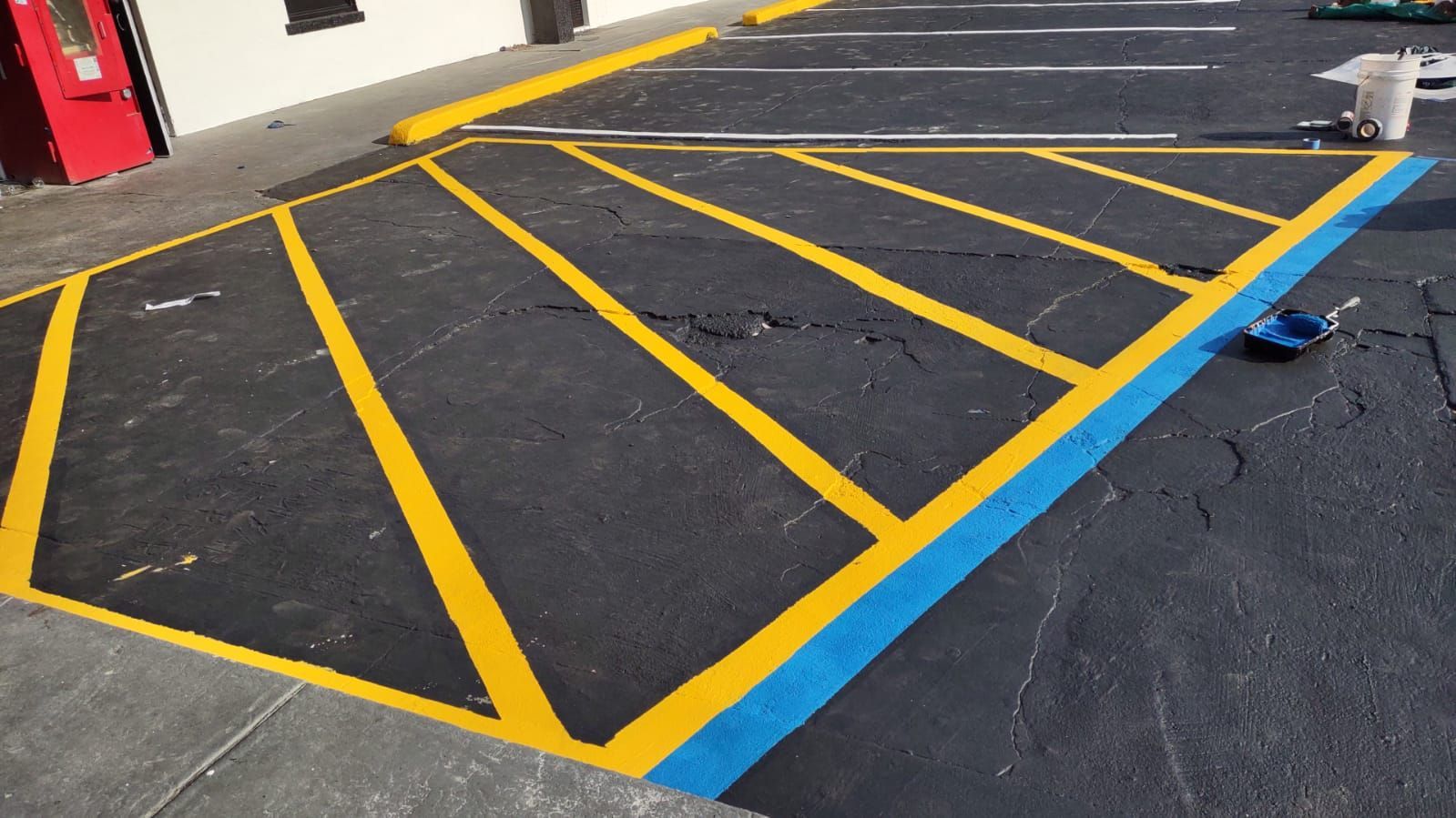 Black asphalt parking area with yellow diagonal lines and a blue curb marking an accessible space