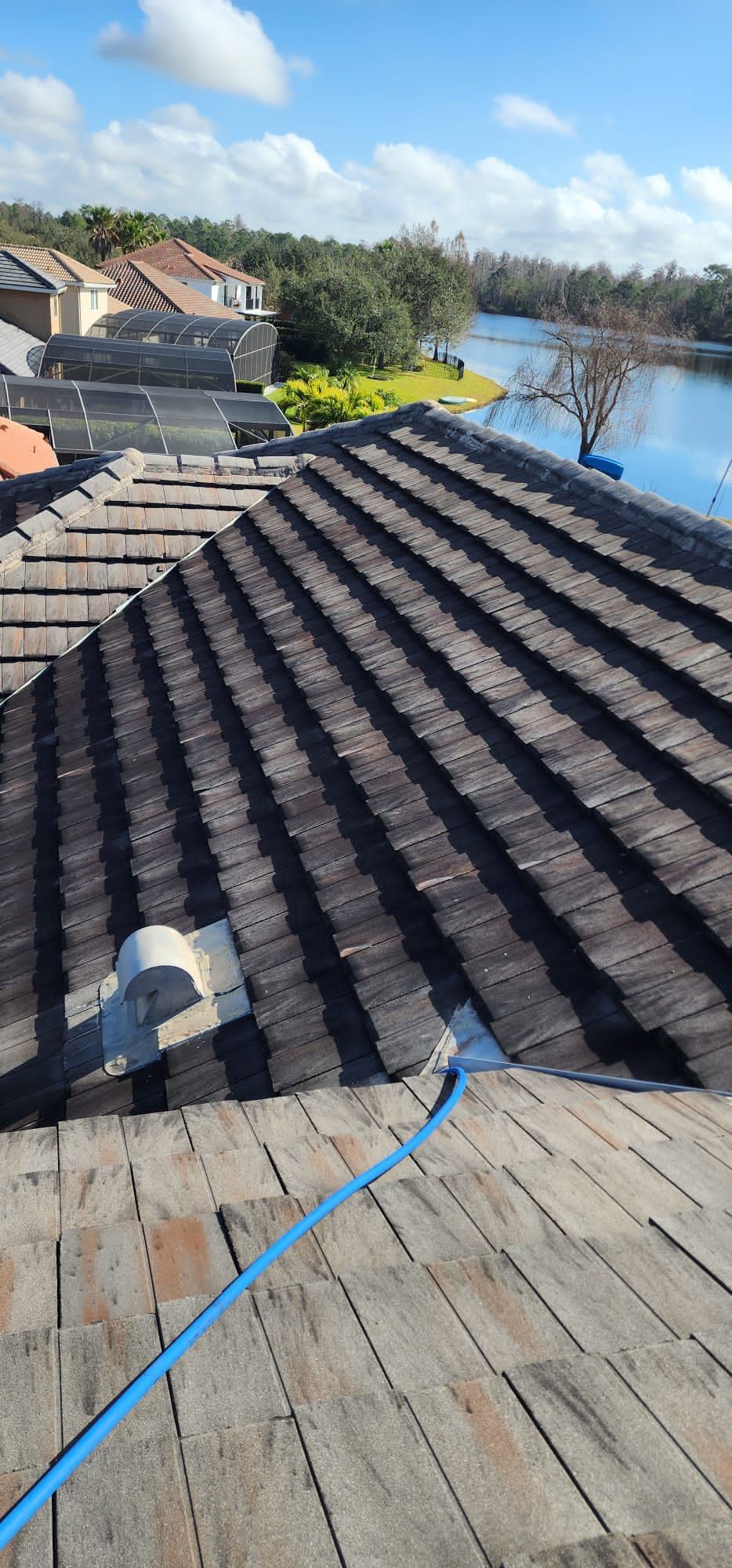 Rooftop with dark gray shingles, blue hose, and a lake view in the distance