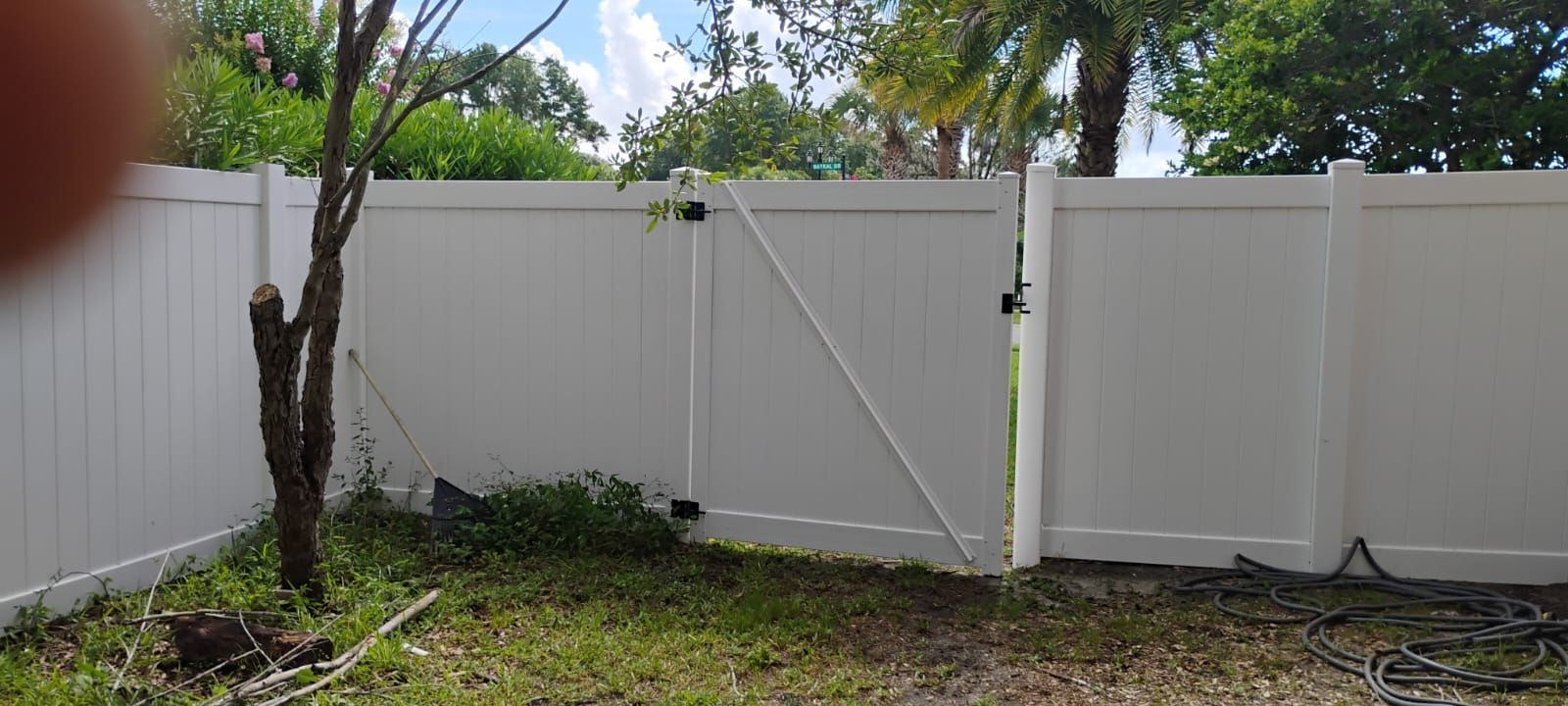White vinyl fence with a gate and tree in a grassy yard under a cloudy sky