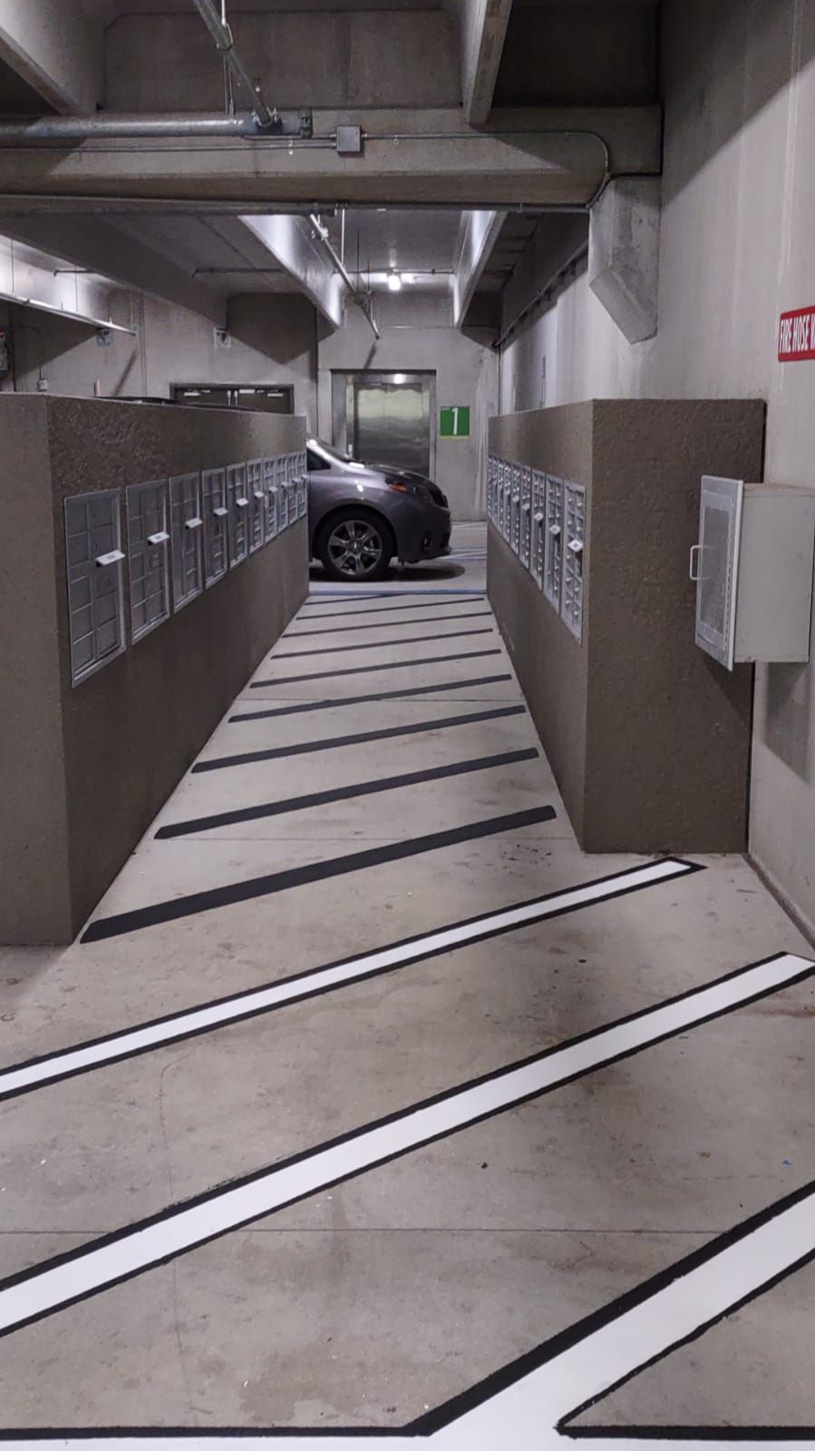 Underground parking garage corridor with metal cabinets, concrete walls, and a car parked at the far end.