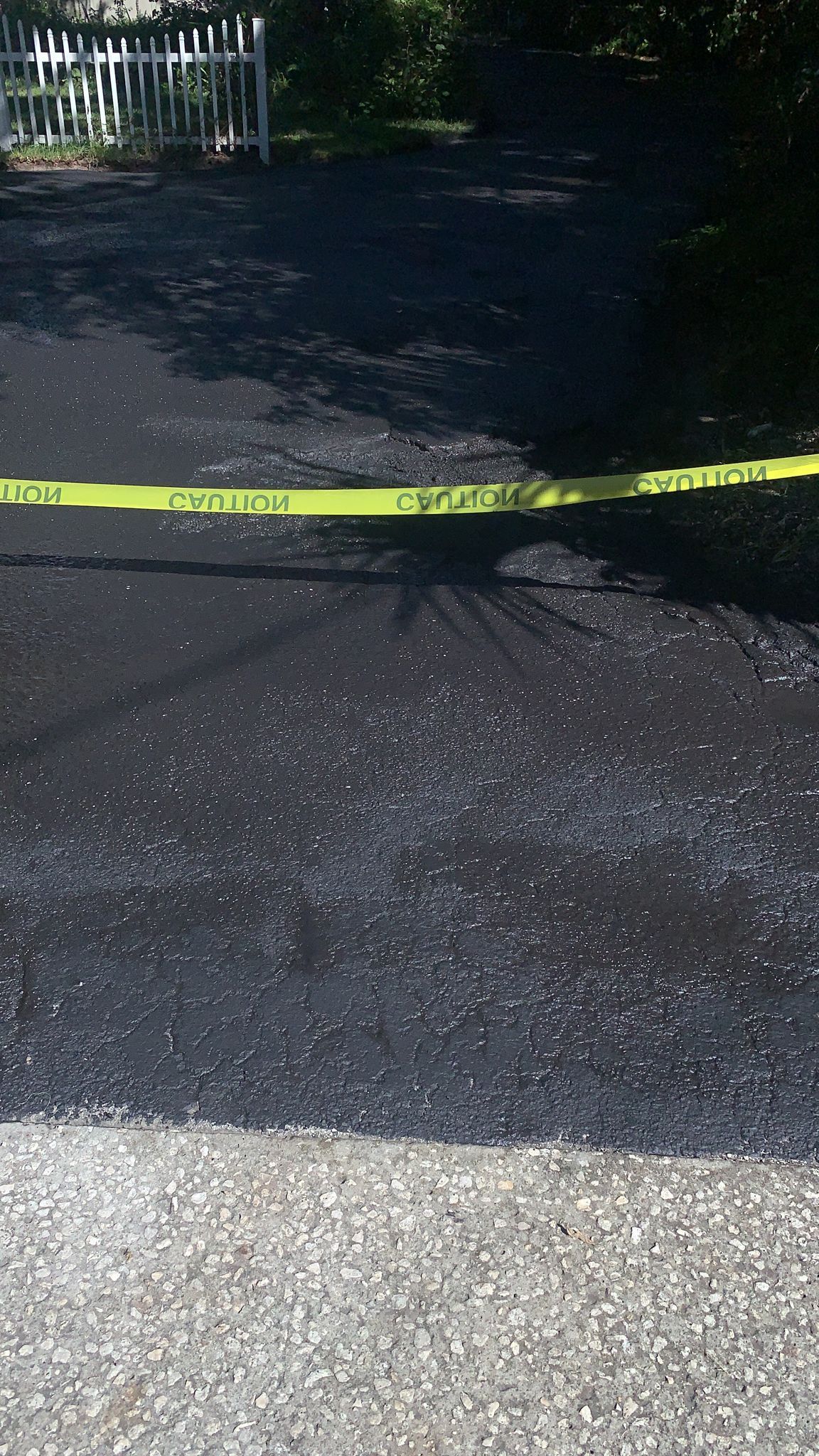 Yellow caution tape stretched across a dark driveway in front of a fenced yard.
