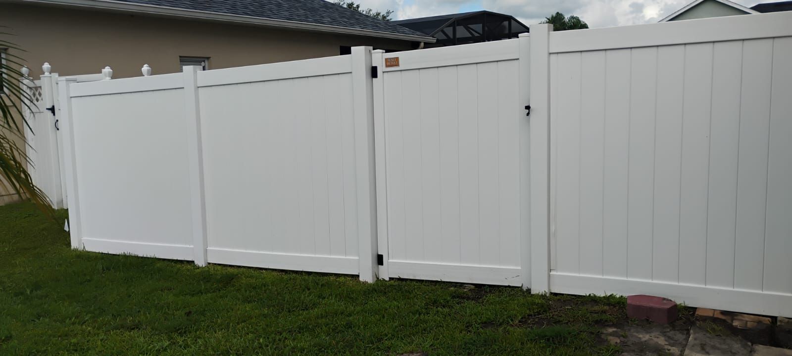 White vinyl fence along a grassy yard beside a house under cloudy skies