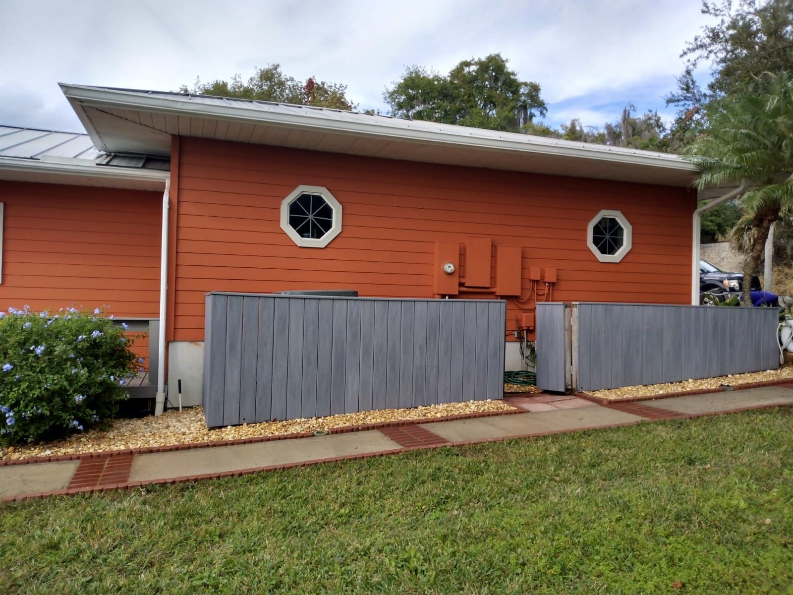 Orange house with white roof, octagonal windows, and gray fence along a grassy yard