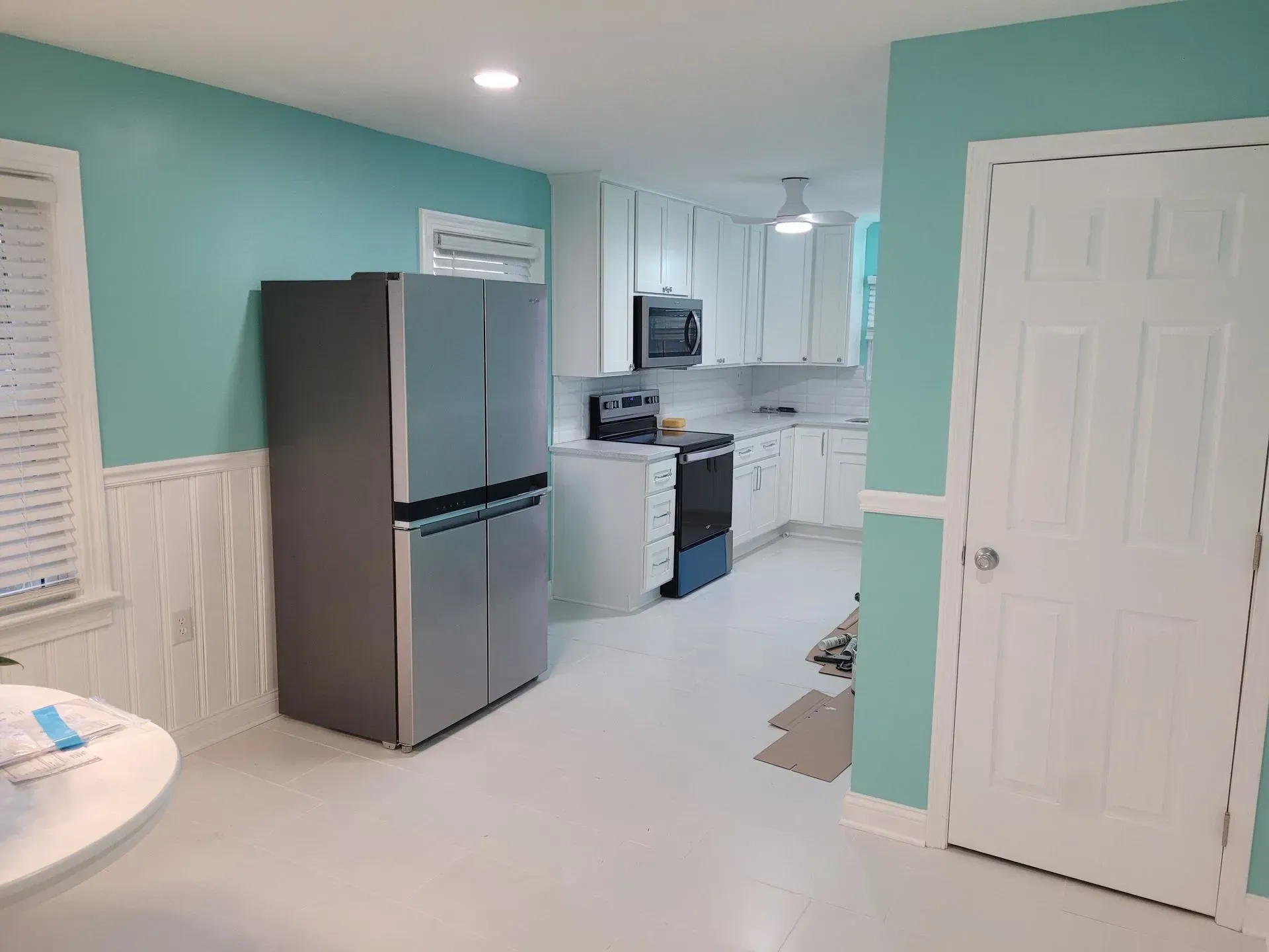 Kitchen with stainless steel refrigerator, white cabinets, teal walls, and white door.