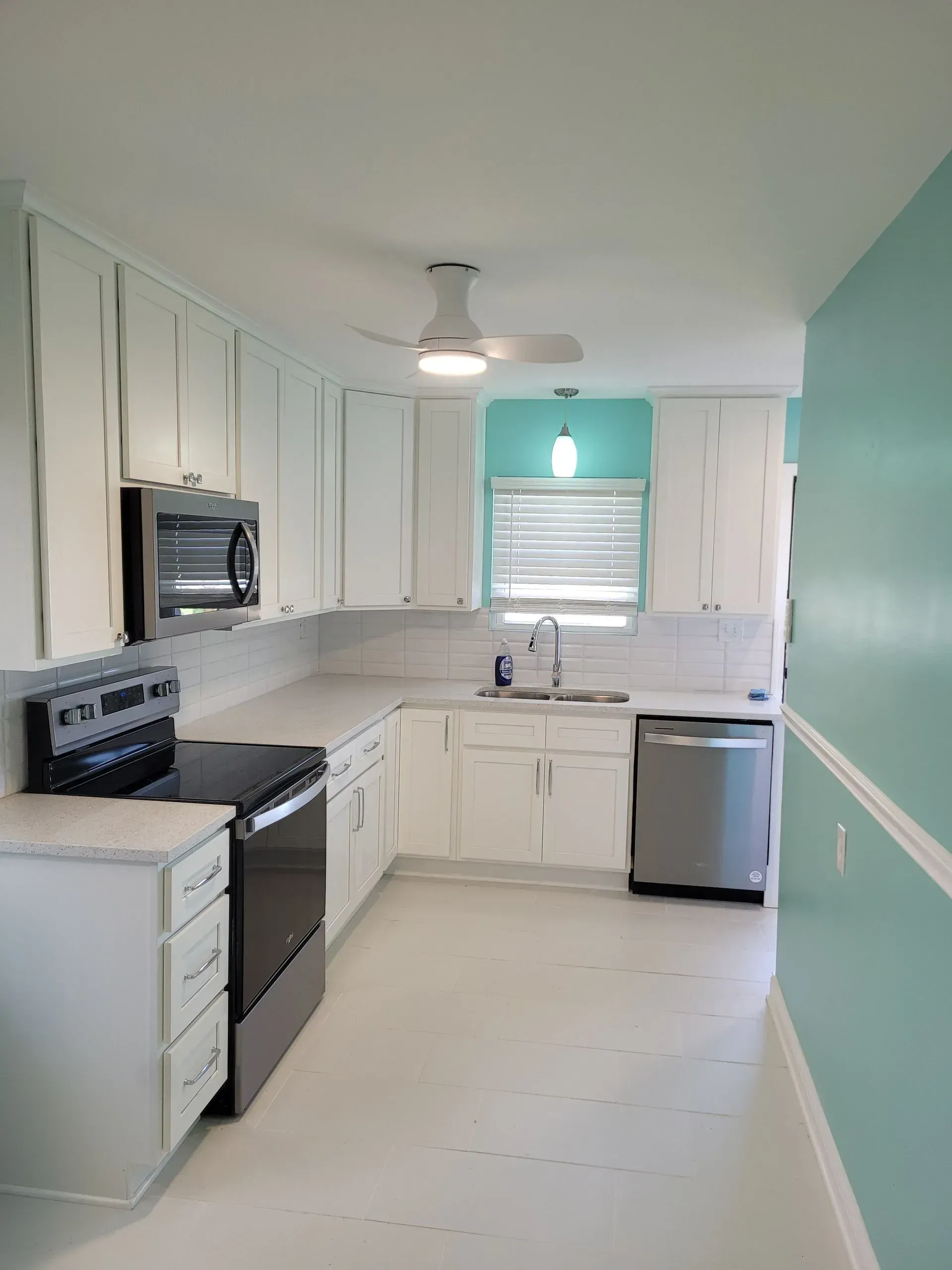 White kitchen with gray appliances, turquoise accent wall, and white cabinets.