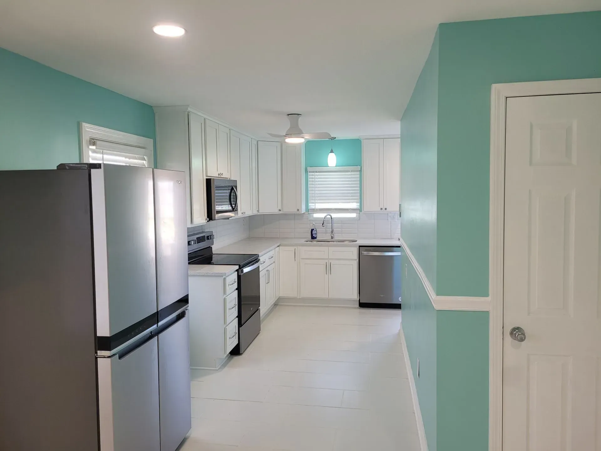 A bright kitchen with teal walls, white cabinets, stainless steel appliances, and white flooring.