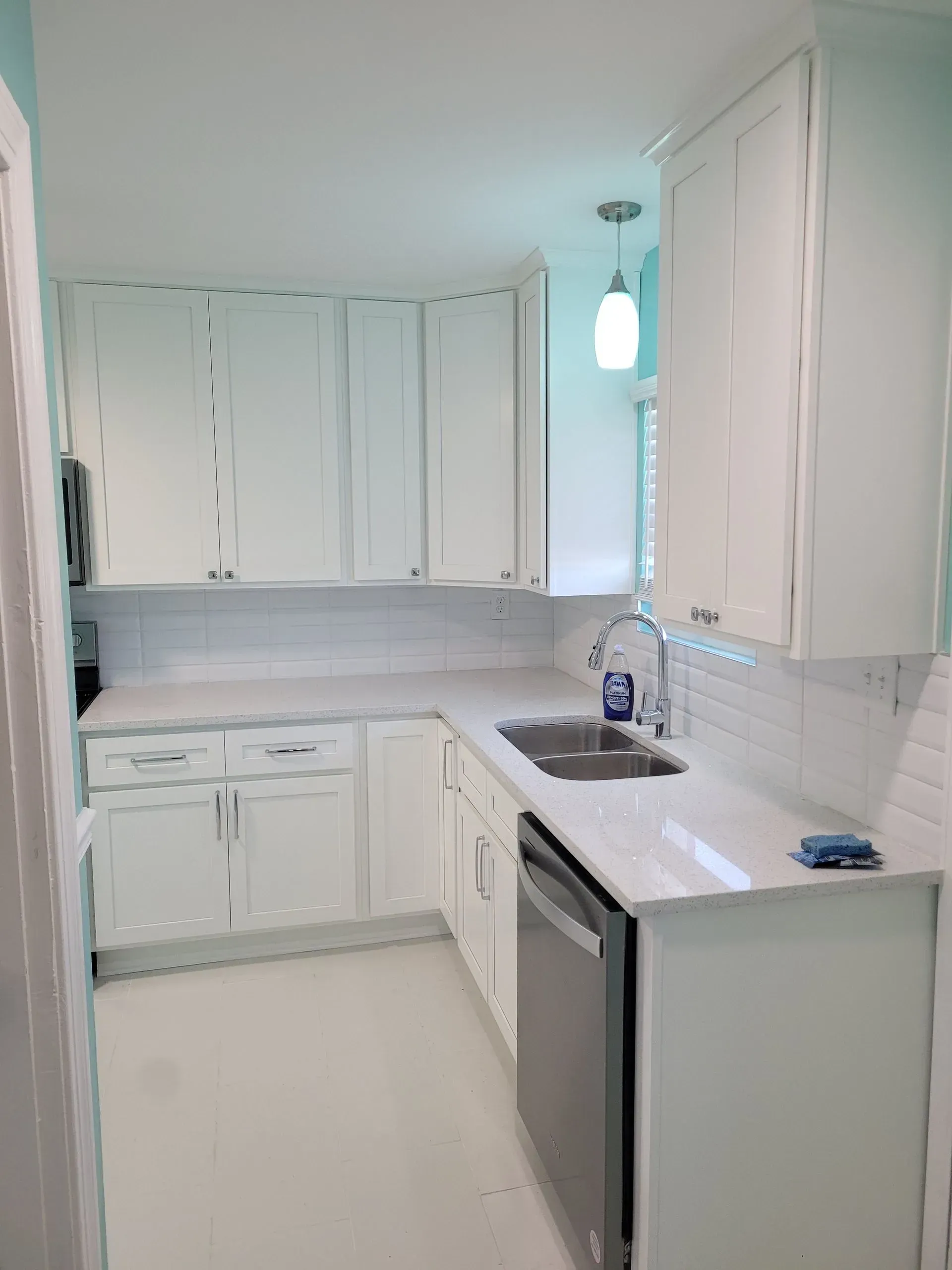 White kitchen with white cabinets, countertops, and backsplash; stainless steel appliances.