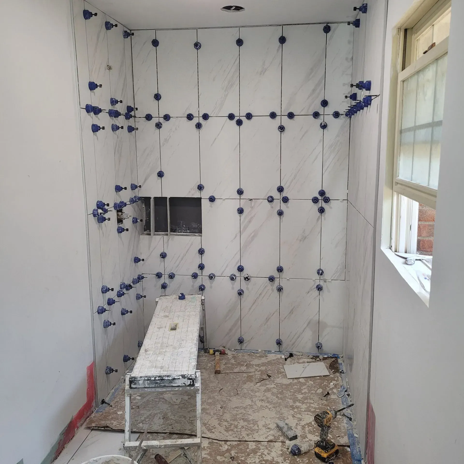 Bathroom with partially tiled walls, tile spacers, and a window.
