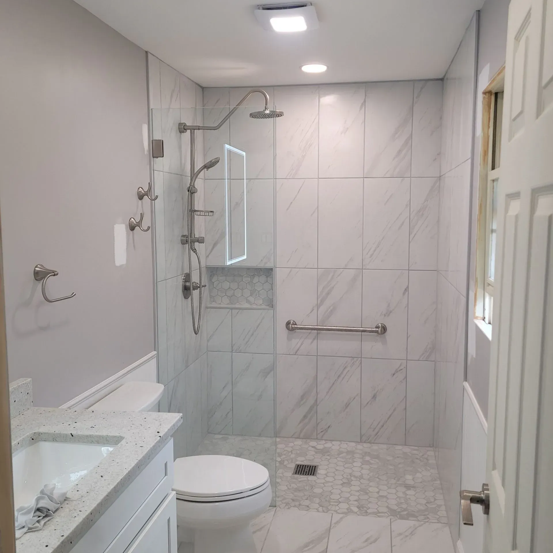 Newly renovated bathroom with a walk-in shower, marble tile, and a grab bar.