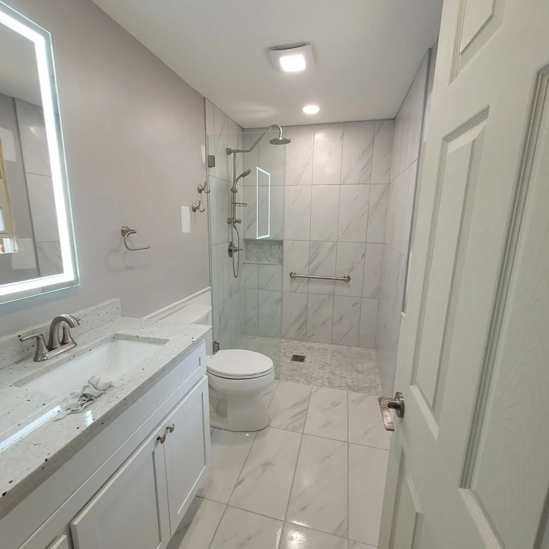 Modern bathroom with white vanity, toilet, and shower with glass doors and grab bar.