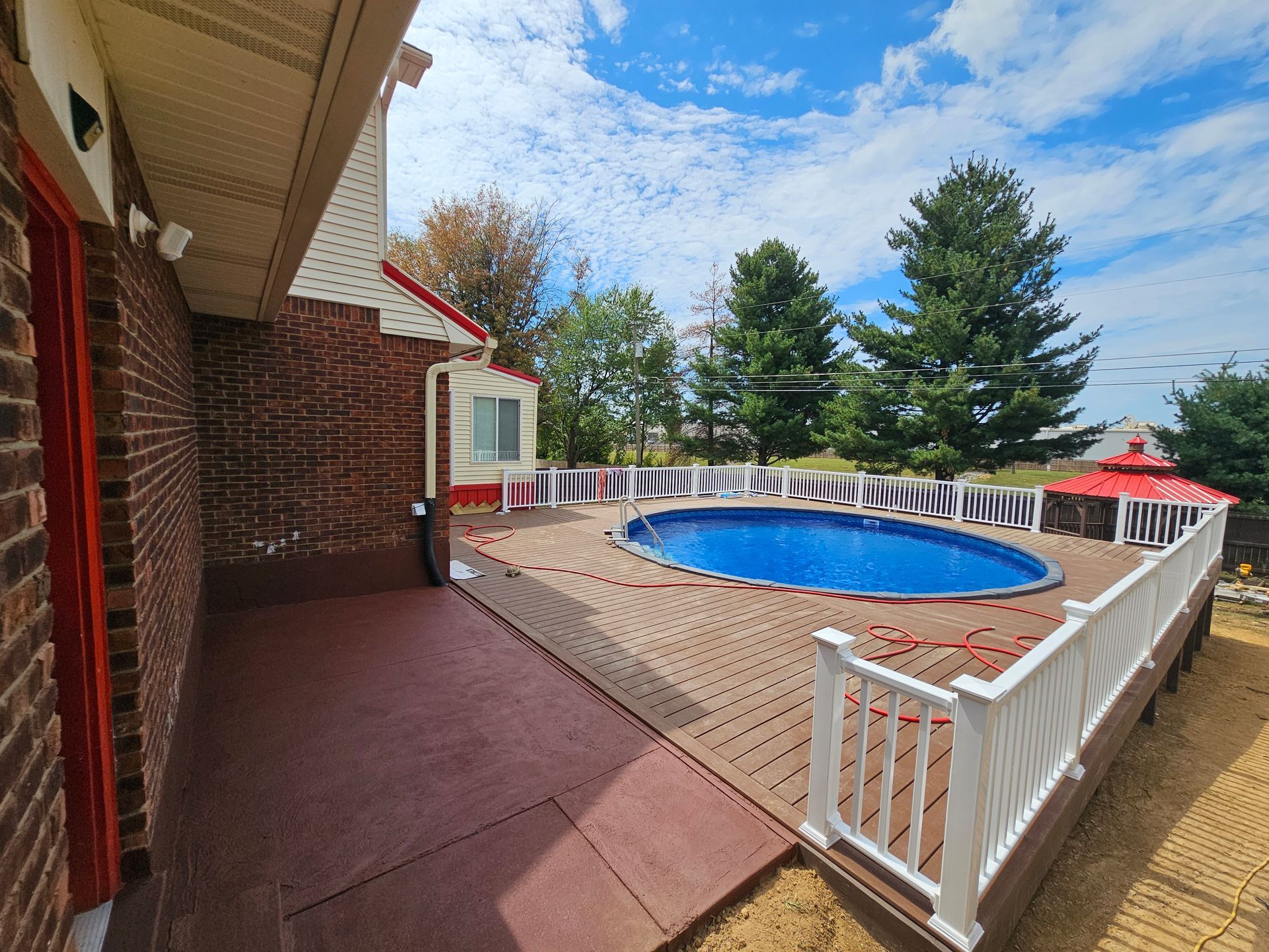 handyman in radcliff ky Brick house with deck and oval pool, white railing, blue sky, green trees.