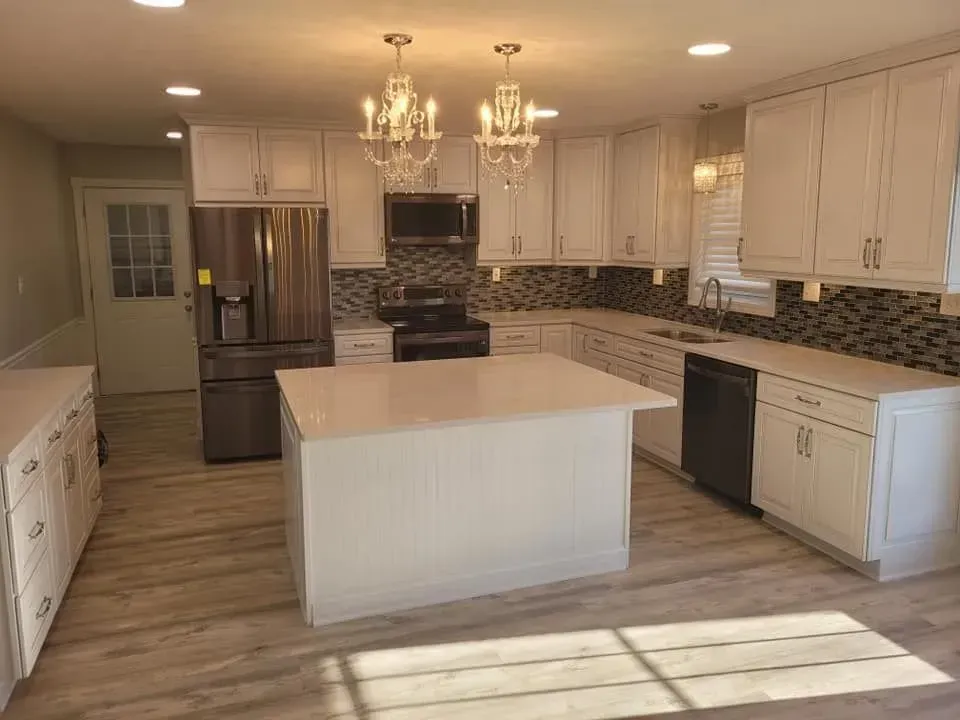 Bright white kitchen with island, stainless steel appliances, light wood floors, and two chandeliers.
