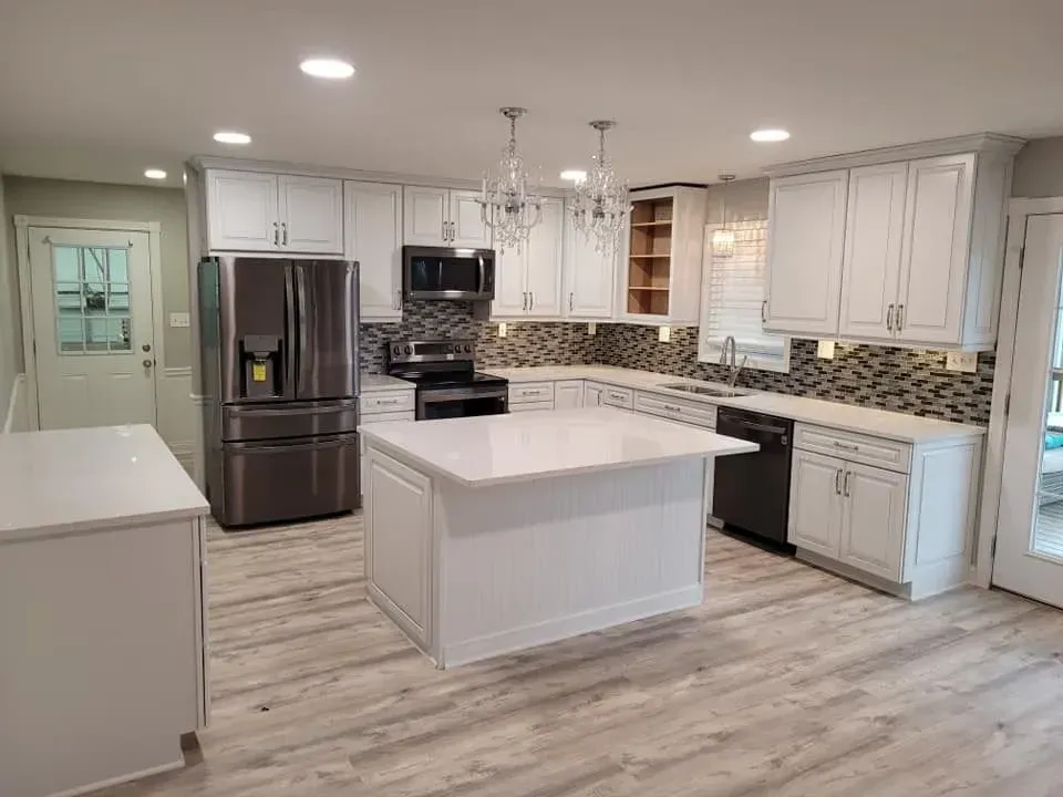 Modern white kitchen with stainless steel appliances, island, and gray wood-look flooring.