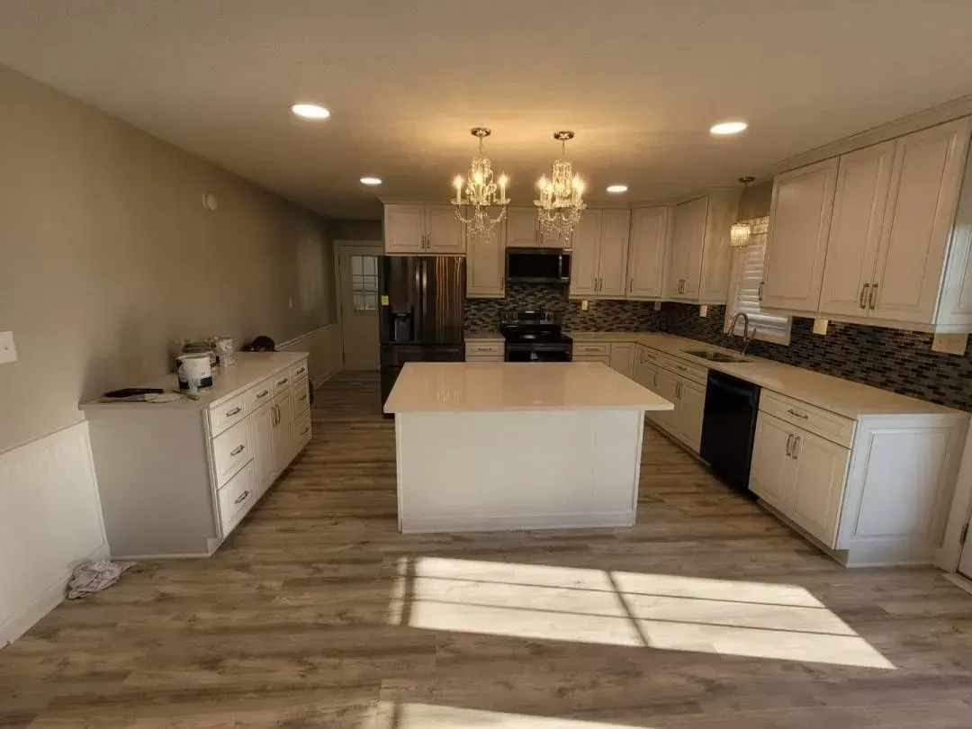 Newly renovated, bright kitchen with white cabinets, island, and chandelier lighting.