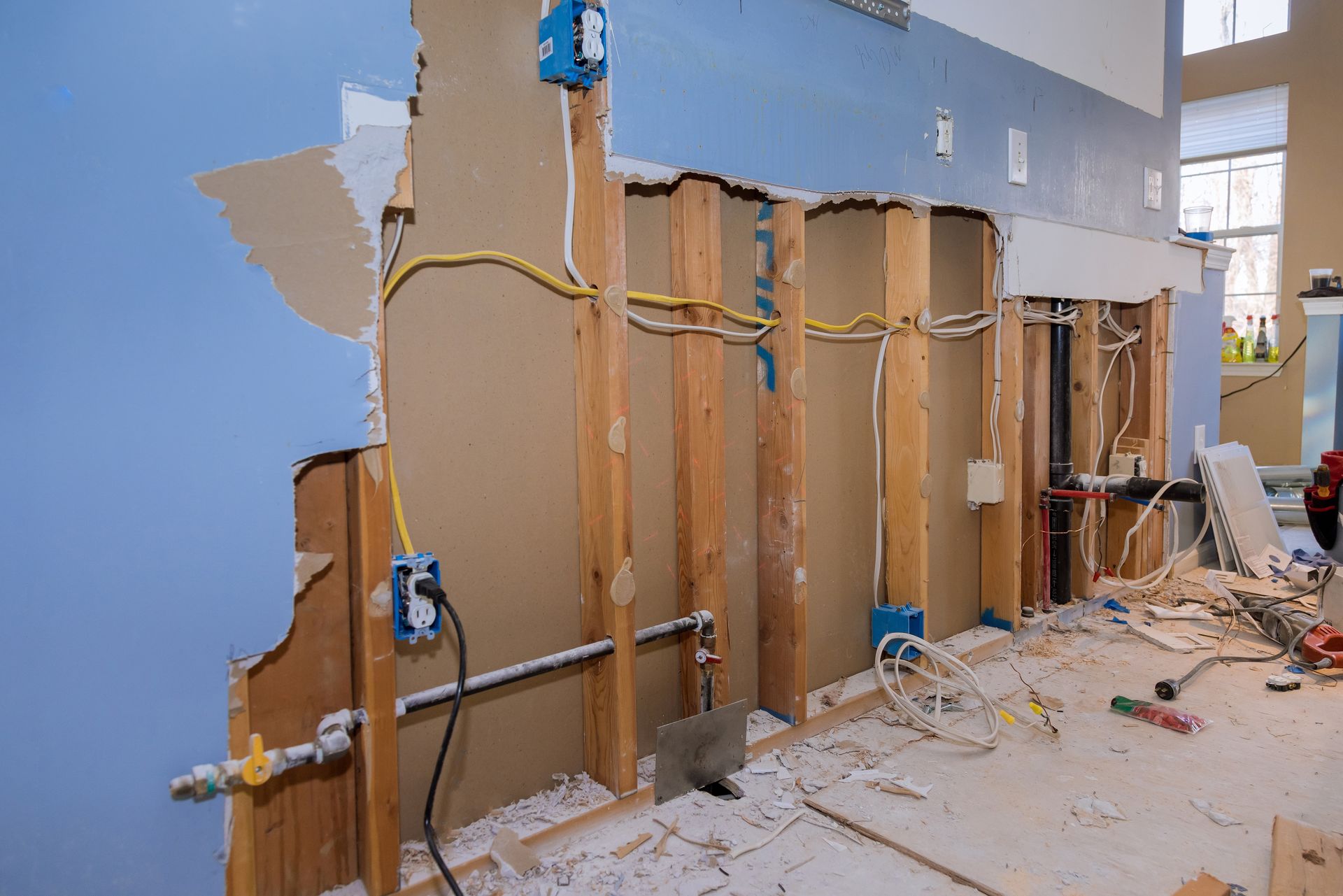 Interior wall during renovation, exposed studs, electrical wiring, and damaged drywall.