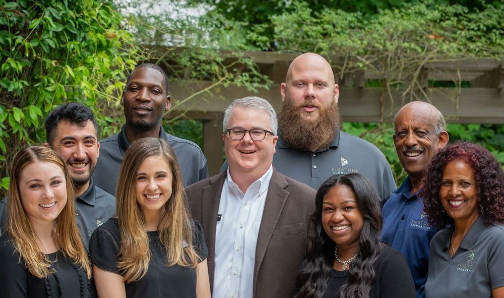 A group of people are standing around a table with laptops.