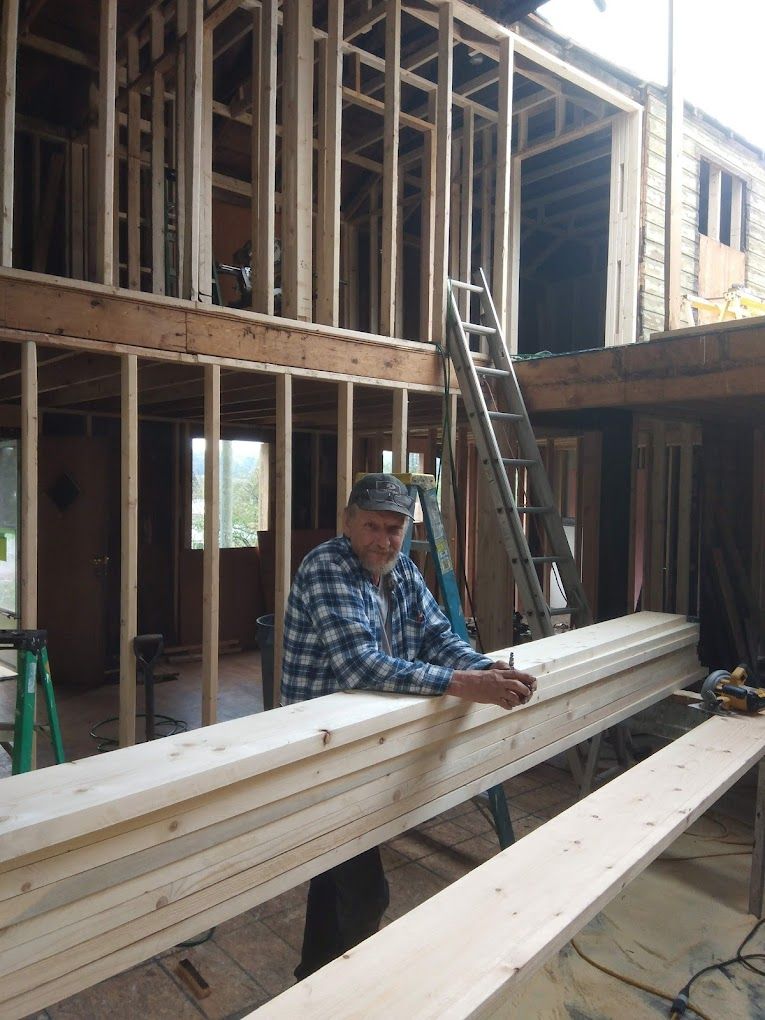 A man in a plaid shirt is leaning on a wooden beam in a building under construction.
