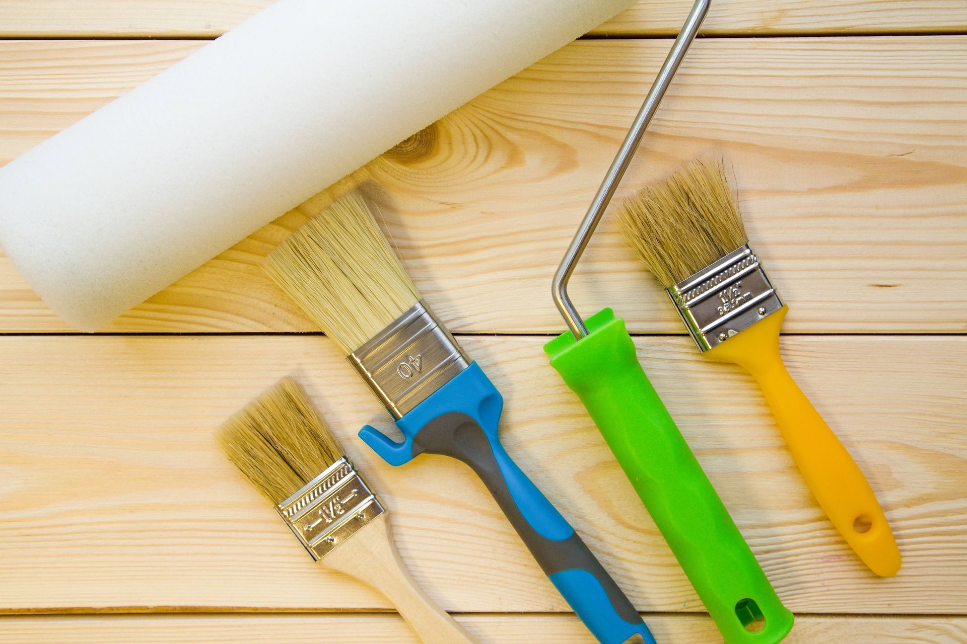 A set of paint brushes and a paint roller on a wooden table.