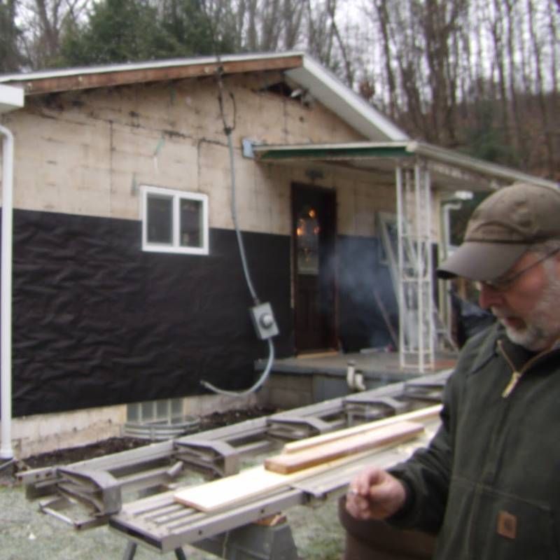 A man standing in front of a house holding a piece of wood