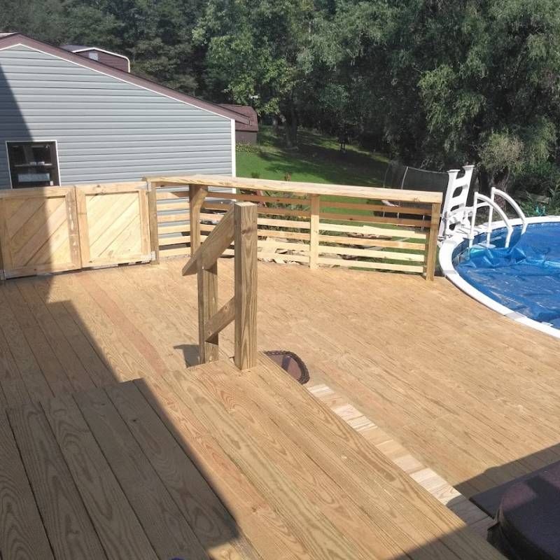 A wooden deck overlooking a swimming pool with a house in the background
