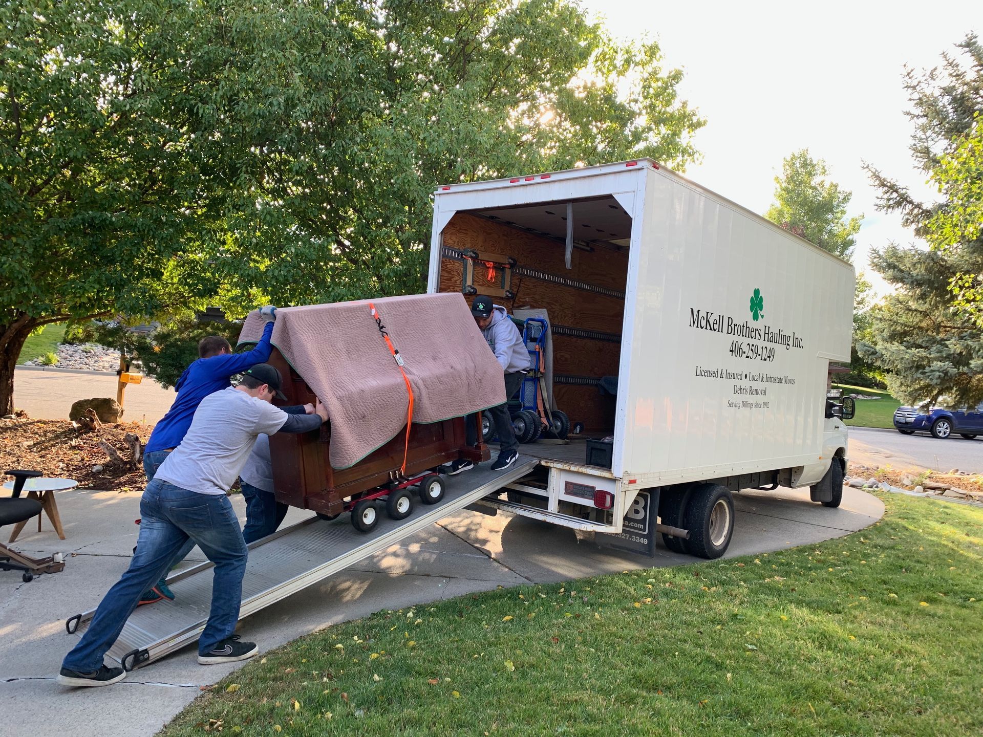 Three people loading a sofa into a moving truck on a driveway.