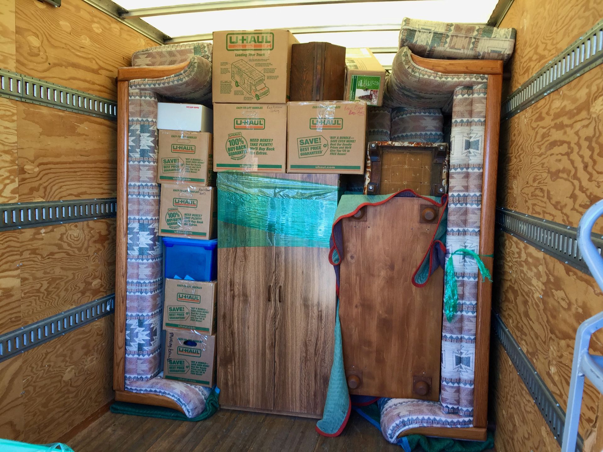 Moving truck filled with boxes, wooden furniture, and rolled rugs.