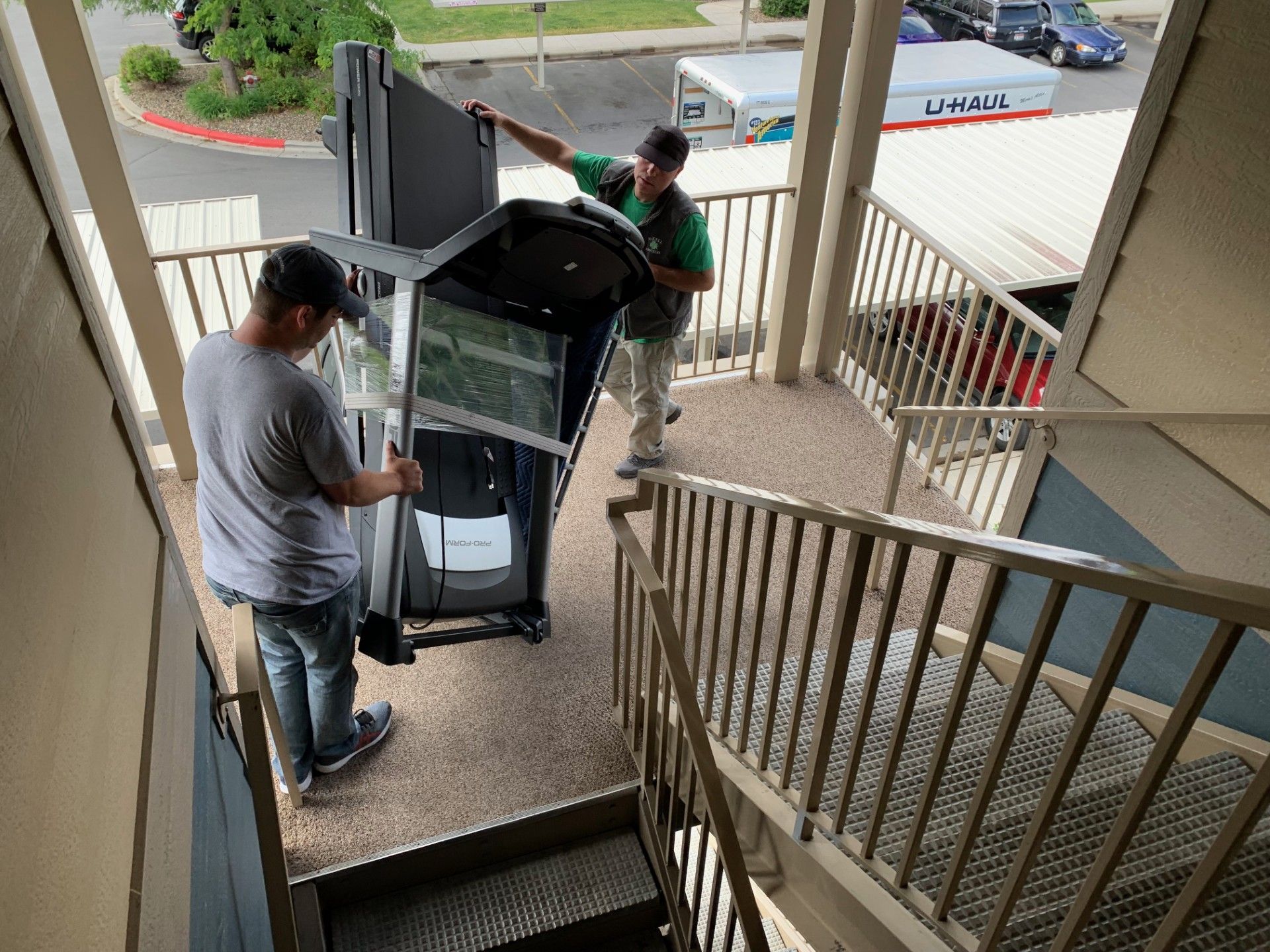 Two people carrying large appliance down outdoor stairs.