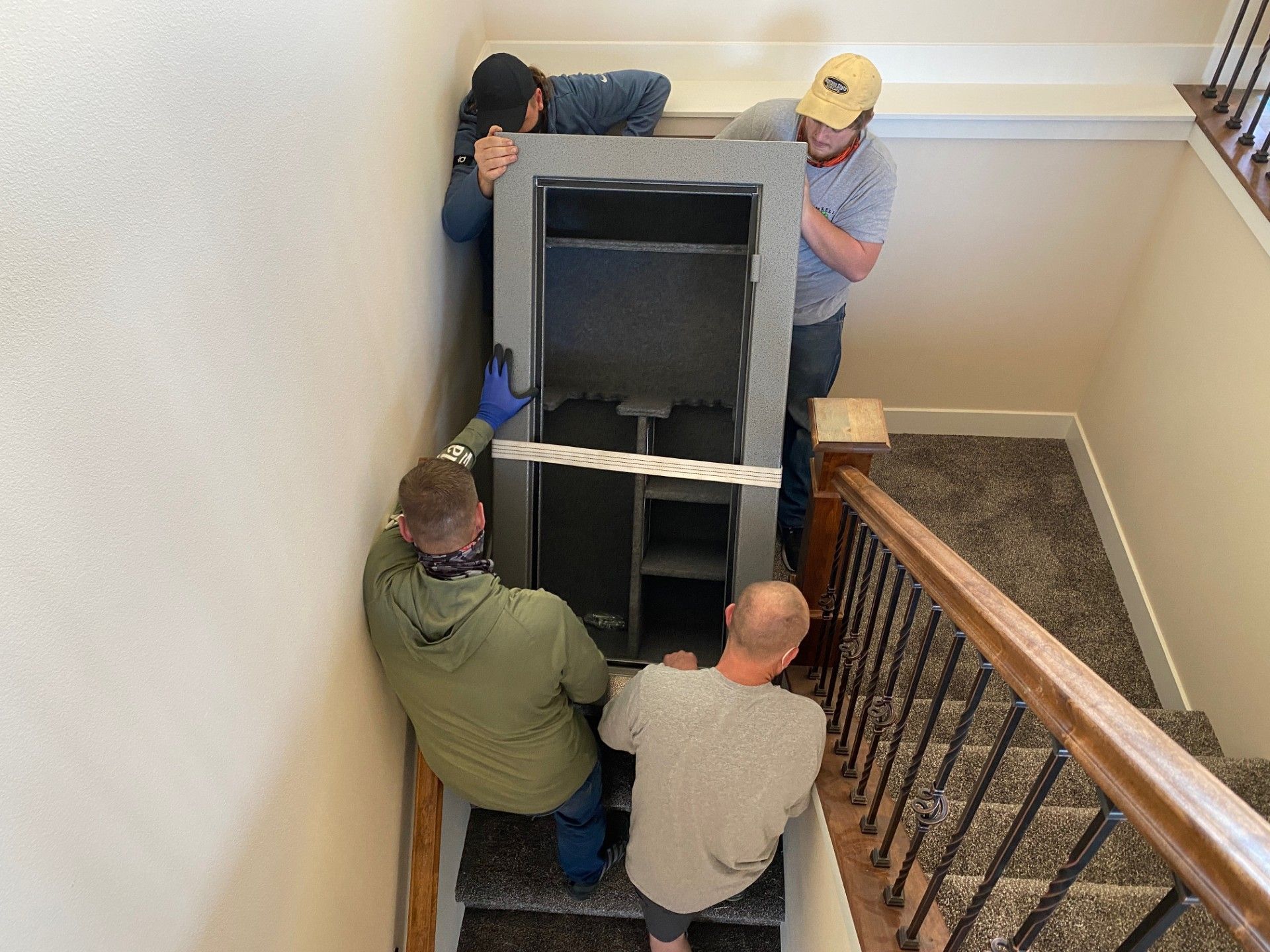 Four people carrying a large safe down carpeted stairs.