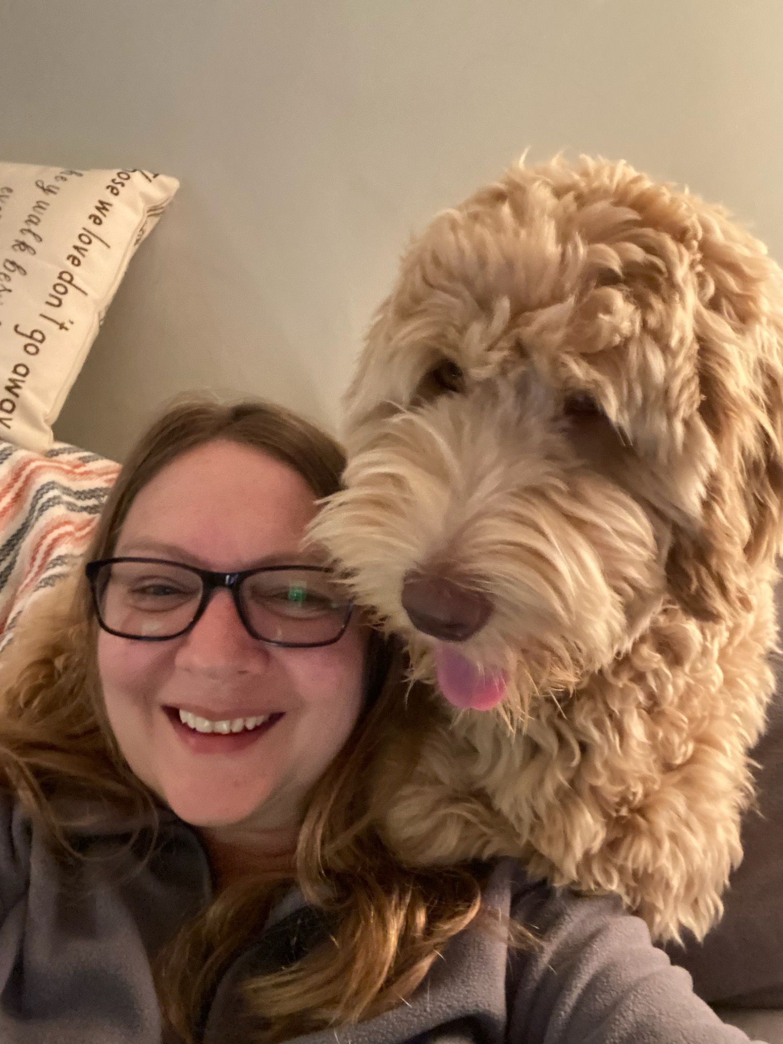 Smiling woman in glasses cuddles a fluffy tan dog on a couch