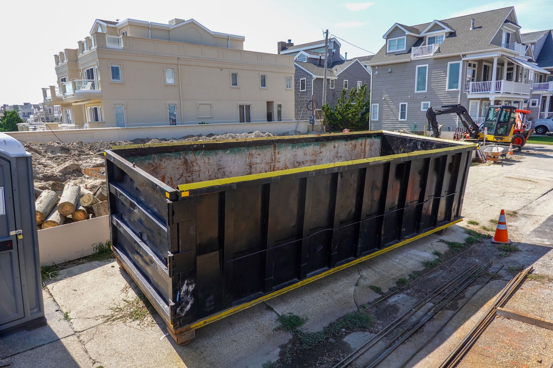 Aerial view of a construction area with trucks, a large dumpster, and piles of debris on dirt ground