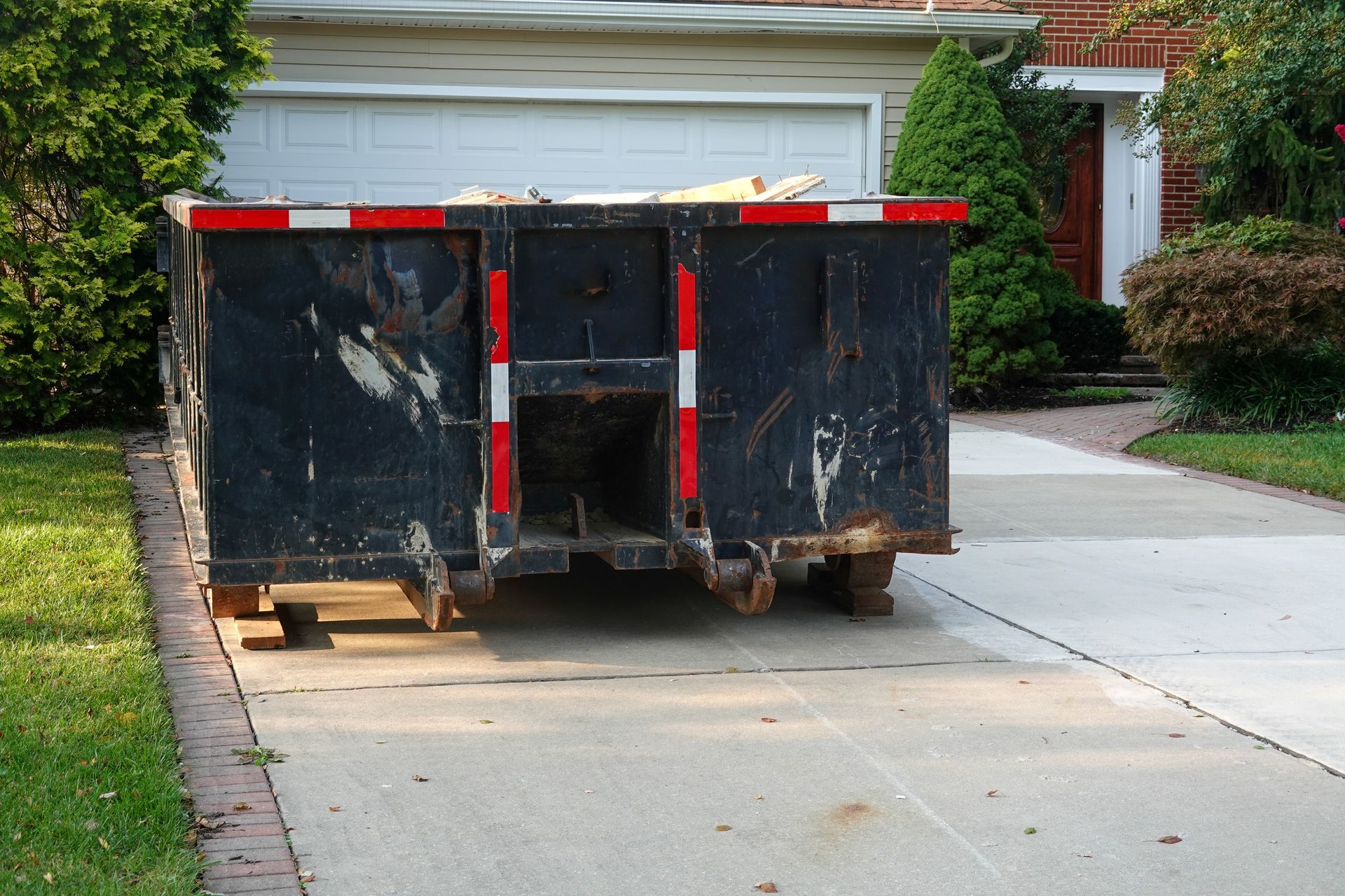 Green dumpster outside a brick storefront with large glass windows