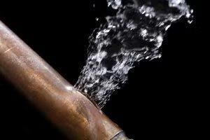 Leaking copper pipe spraying water against a black background