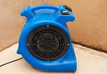 Blue air mover blower fan on a floor against a wall