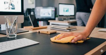 Hand wiping a black desk with a yellow cloth in a modern office workstation