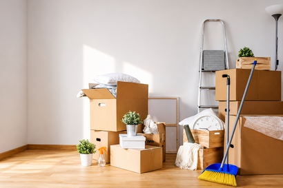 Moving boxes and cleaning tools in a sunlit empty room with wooden floors