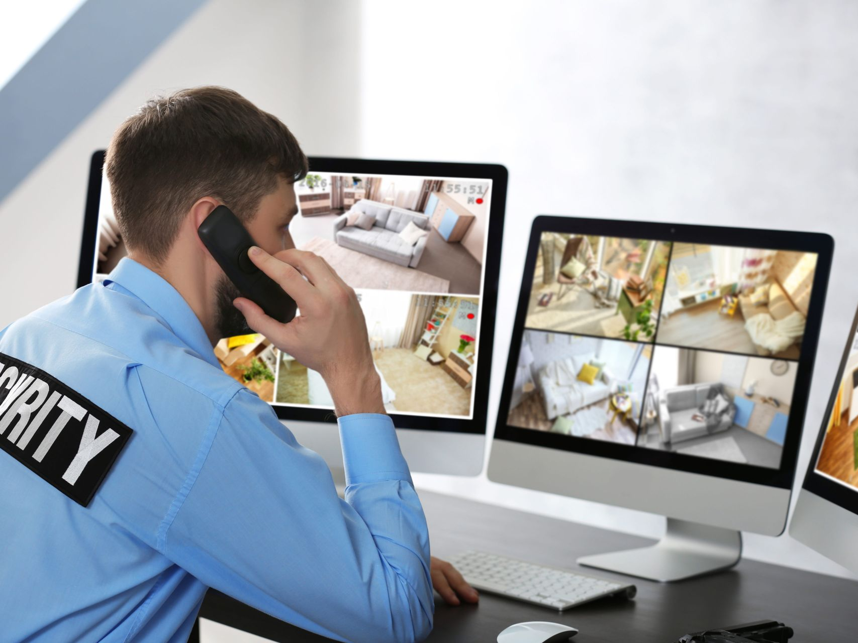 Security guard on phone monitoring multiple CCTV screens in a control room.