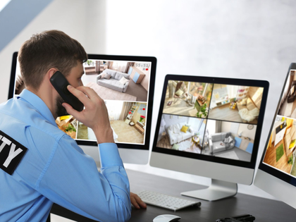 Security guard monitoring CCTV cameras at a desk and speaking on a phone