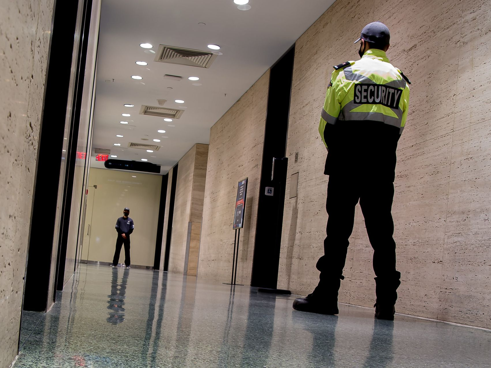 Security guards standing in a hallway, one in a neon yellow jacket in the foreground.