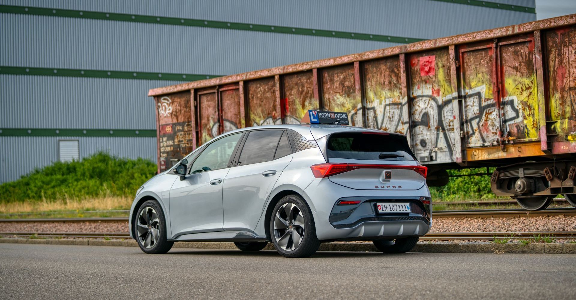 Neben einem mit Graffiti besprühten Zugwaggon steht ein silbernes Auto.